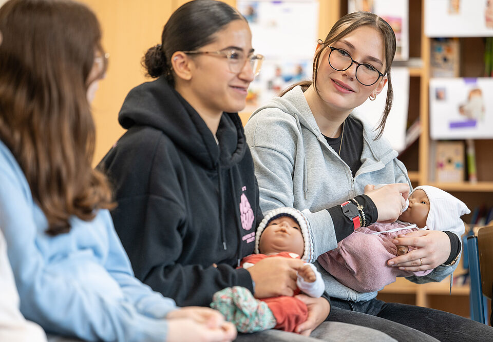 Drei Schülerinnen mit Babypuppen im Arm