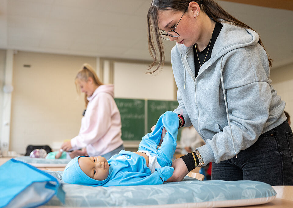 Zwei Schülerinnen wickeln ihre Babypuppen