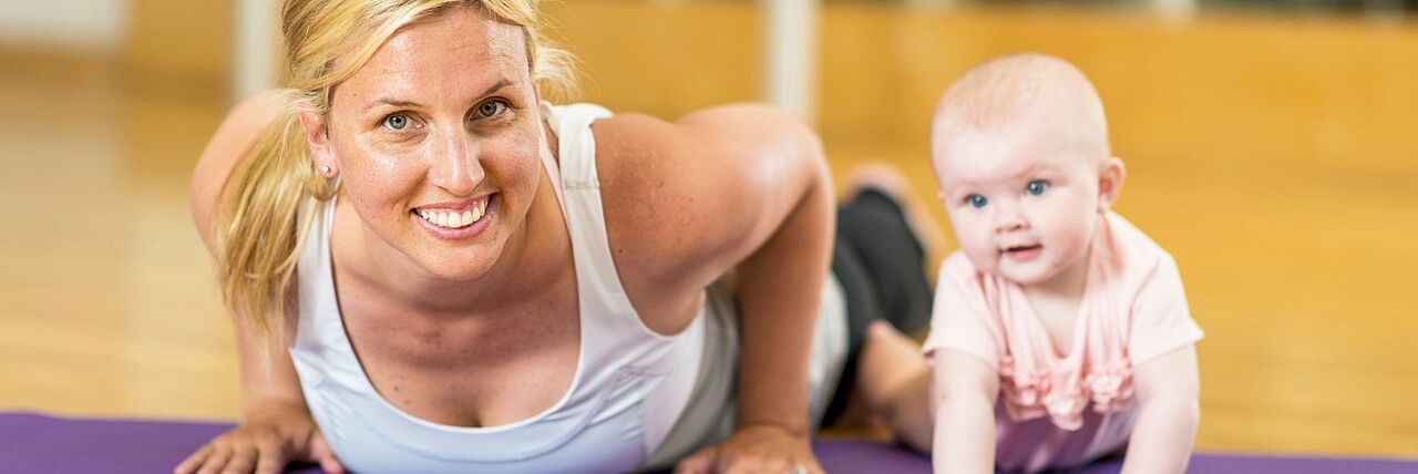Mutter- Kind Kurse Mutter liegt mit Baby auf Yogamatte